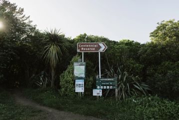 Juvenile Delinquent track entrance with five signs showing a park map, safety warnings, directions to Centennial Reserve and the pump track.