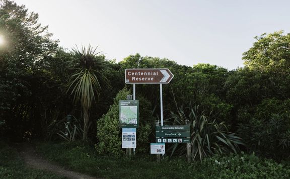 Juvenile Delinquent track entrance with five signs showing a park map, safety warnings, directions to Centennial Reserve and the pump track.