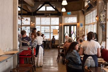 The warm interior of Ombra on Cuba Street. A waiter waits tables and people enjoy their meals under the yellow lights.