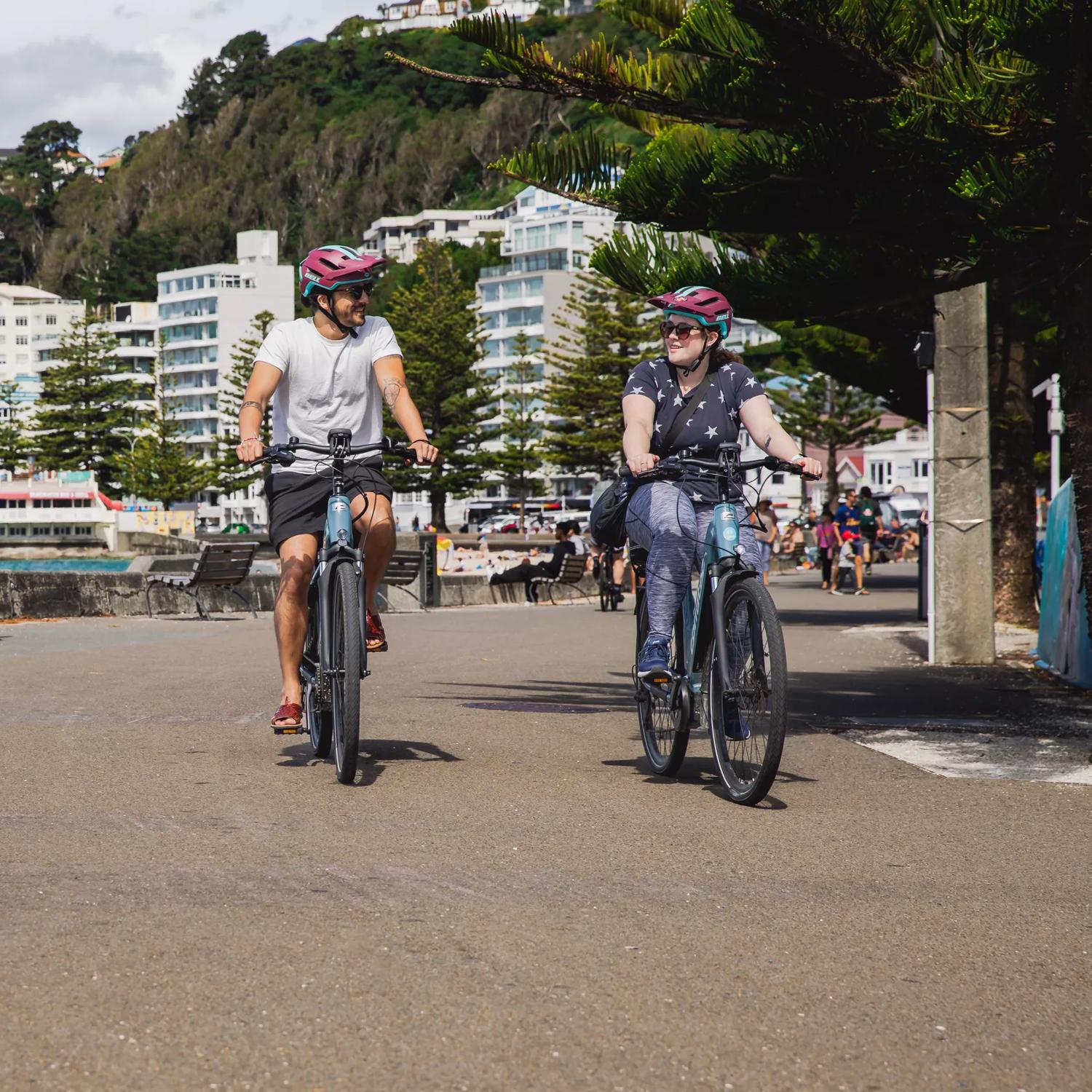 Two people ride bicycles along Oriental Parade.