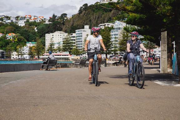 Two people ride bicycles along Oriental Parade.