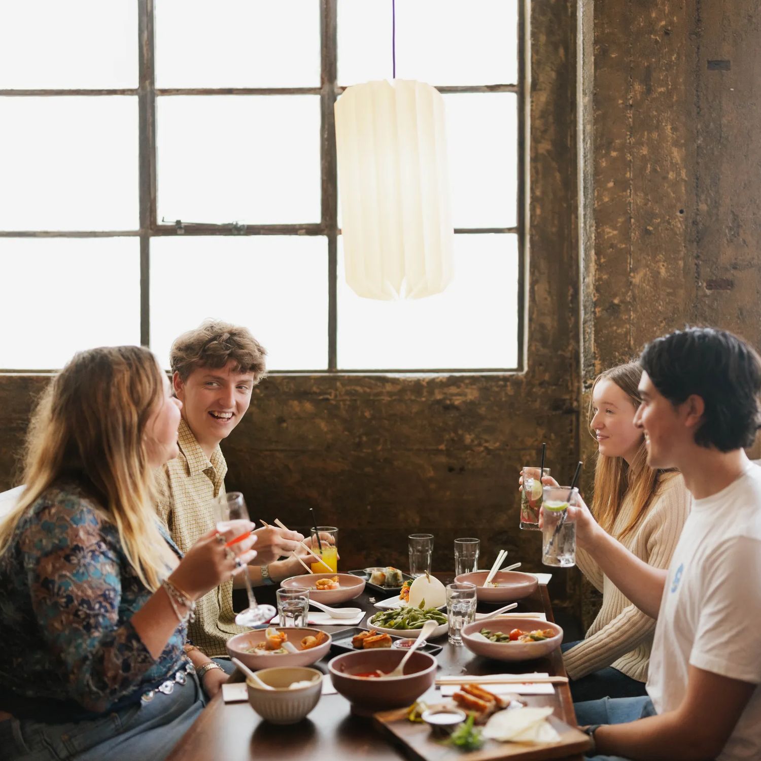 Four young adults enjoy drinks and food in a booth table under a large window inside Chow, on Tory Street.