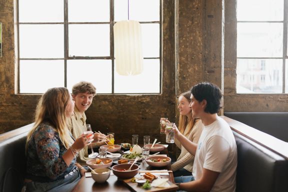 Four young adults enjoy drinks and food in a booth table under a large window inside Chow, on Tory Street.
