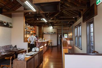 Inside Rosella looking at the upstairs restaurant and bar. Two bar staff are standing behind the bar and windows line the right hand wall.