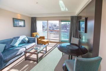 Interior of room at the Copthorne hotel, with a blue couch, coffee table, circular dining table with chairs and tv. Floor to ceiling windows look out over the city.