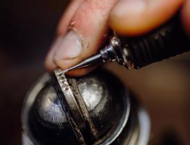 Super close-up of fingers drilling small holes into a handmade ring at Rawson Brothers Jewellery in Upper Hutt.