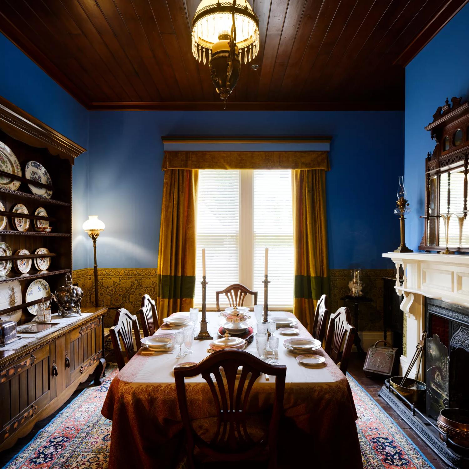 The dining room of Katherine Mansfields house with blue painted walls and a dinner setting on the table.