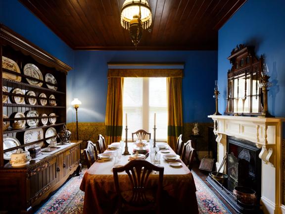 The dining room of Katherine Mansfields house with blue painted walls and a dinner setting on the table.