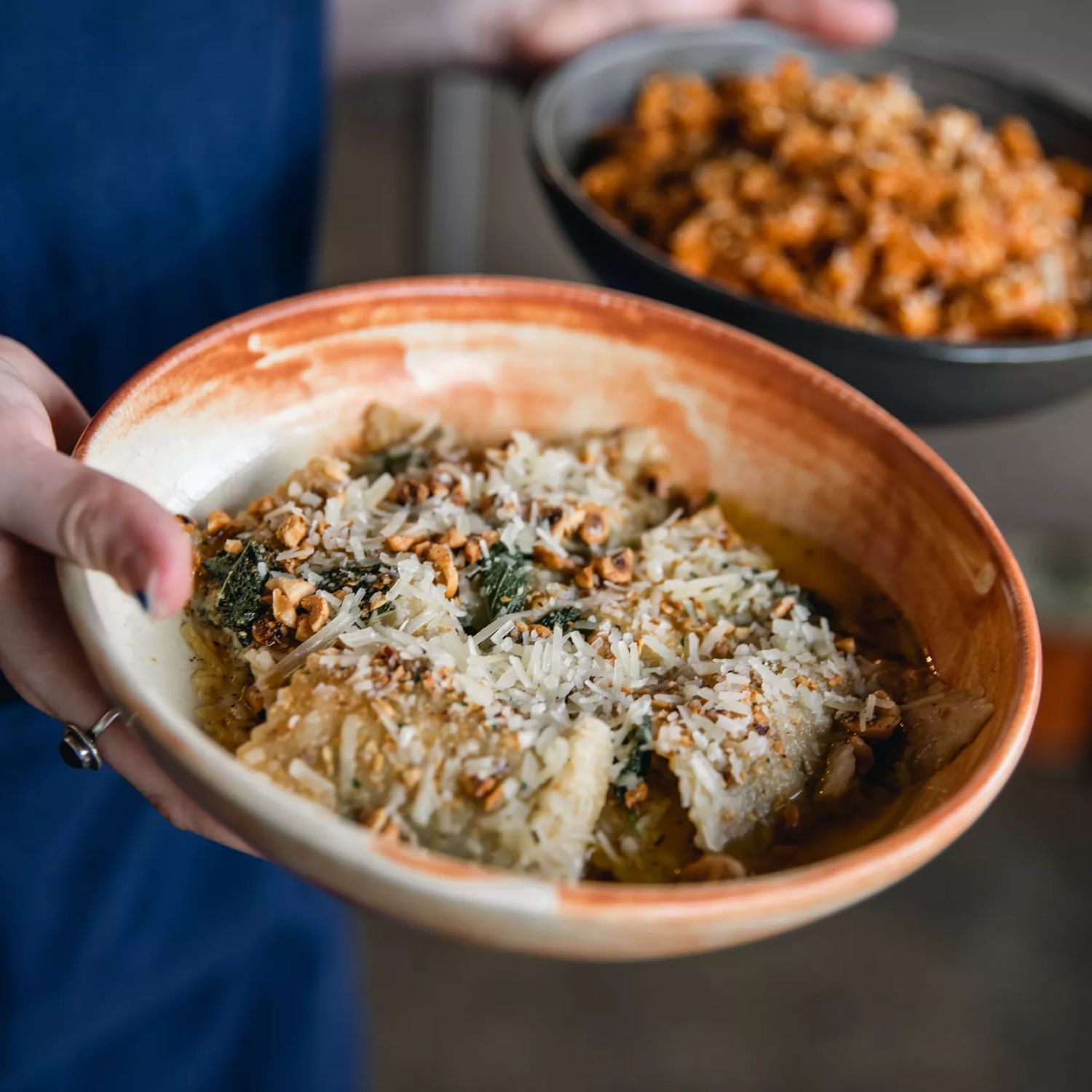 Close-up of waiters hands holding two pasta bowls at 1154 Pastaria on Cuba Street. Focused in the foreground is ravioli.