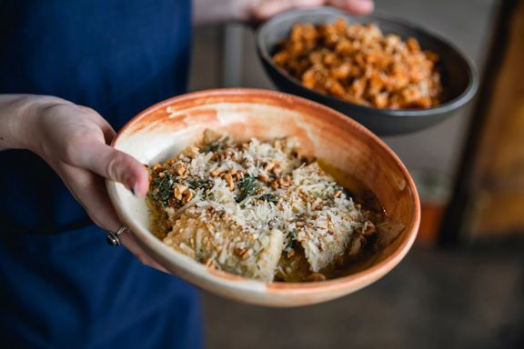 Close-up of waiters hands holding two pasta bowls at 1154 Pastaria on Cuba Street. Focused in the foreground is ravioli.