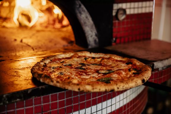 A pizza at Pizza Pomodoro going into a fire oven.