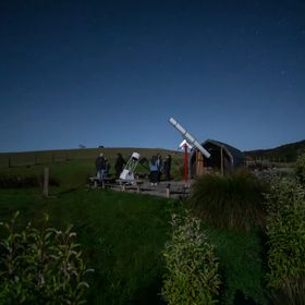 People standing next to a telescope at night at the Star Safari experience in Carterton.