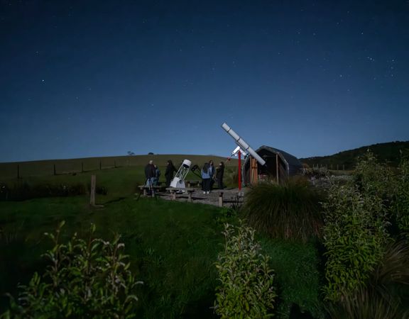 People standing next to a telescope at night at the Star Safari experience in Carterton.