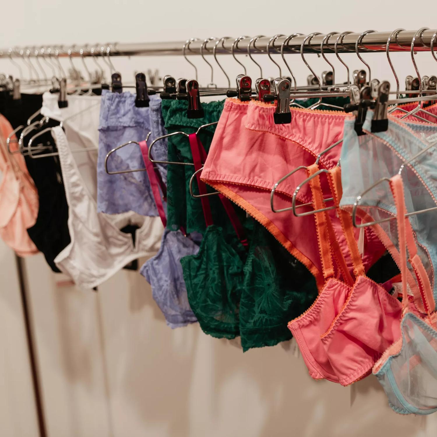 High-end undergarments hang on metal hangers at a lingerie shop.