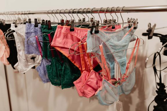 High-end undergarments hang on metal hangers at a lingerie shop.