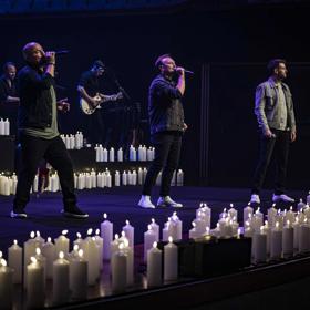 Three singers and two supporting musicians perform a candlelit concert.