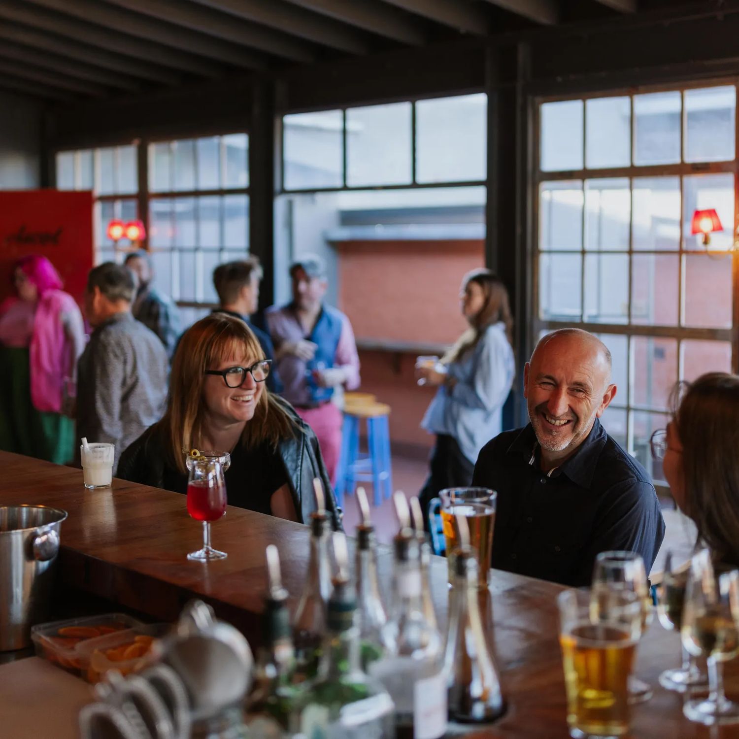 Three people at Ascot sitting at the bar, while a server makes cocktails.