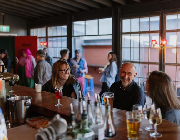 Three people at Ascot sitting at the bar, while a server makes cocktails.