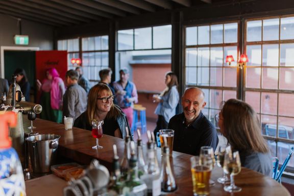 Three people at Ascot sitting at the bar, while a server makes cocktails.