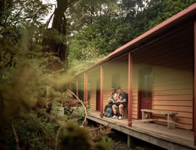 Two people sit outside the historic whare — the oldest nature conservation building in New Zealand, on Kapiti Island.