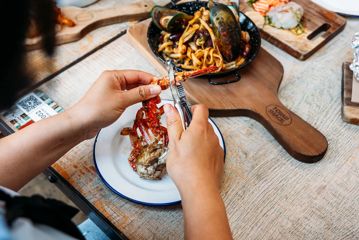 A person uses a metal tool to crack into a crab leg while eating at The Crab Shack.