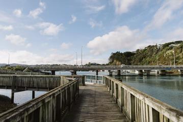 A wooden path above water turns to the left under a blue sky with scattered clouds.