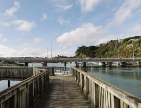 A wooden path above water turns to the left under a blue sky with scattered clouds.