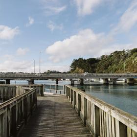 A wooden path above water turns to the left under a blue sky with scattered clouds.