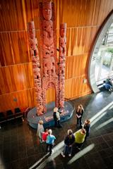 A group stand in a semi-circle while looking at a tall Māori sculpture at the Museum of New Zealand Te Papa Tongarewa in Wellington.