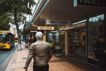 A person walking on a city street in front of a store called 'Unity Books'.