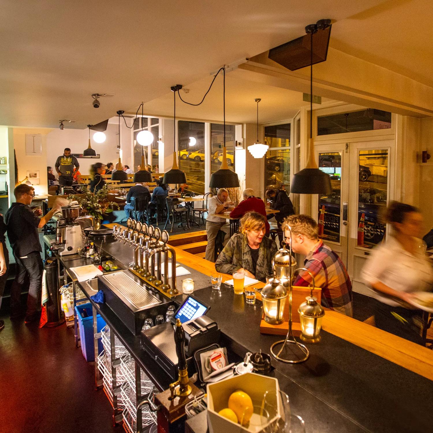 Inside a busy low-lit pub of people enjoying food and drinks. 