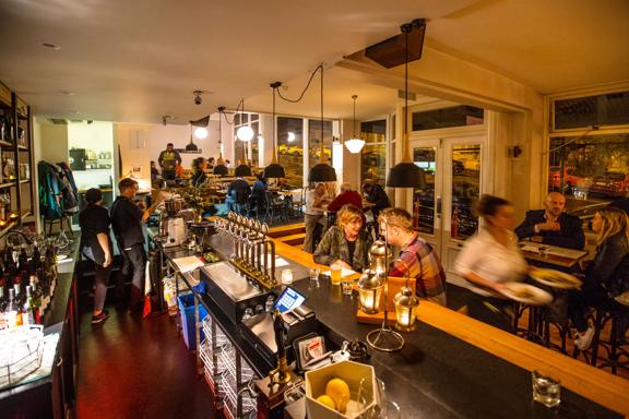 Inside a busy low-lit pub of people enjoying food and drinks. 