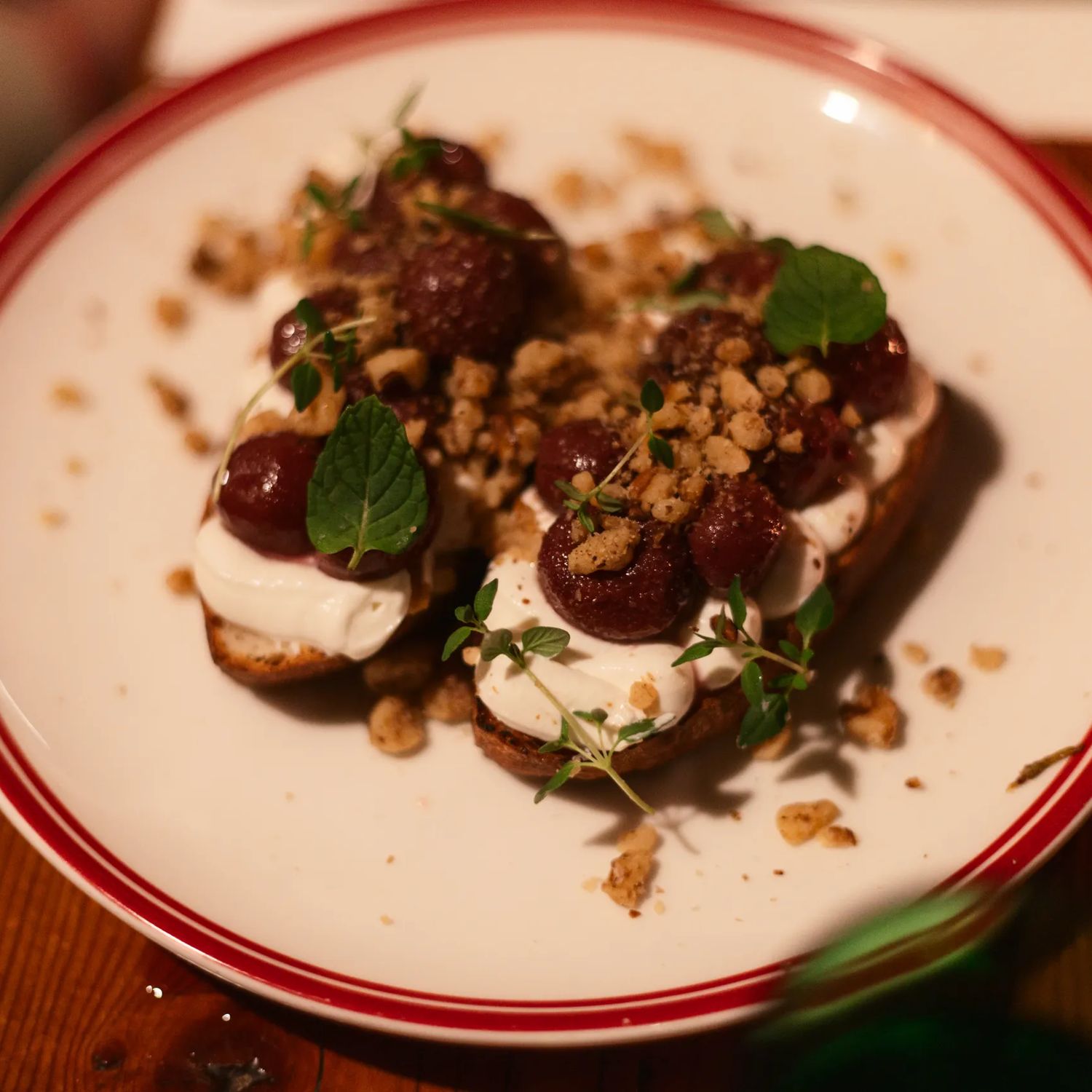 Plate of dessert topped with dollops of cream, caramelized fruit, crushed nuts, and fresh mint leaves, served on a restaurant table.