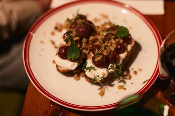Plate of dessert topped with dollops of cream, caramelized fruit, crushed nuts, and fresh mint leaves, served on a restaurant table.