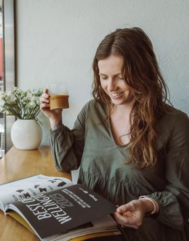 A person drinks an iced coffee while reading a magazine by the front window at Customs café.