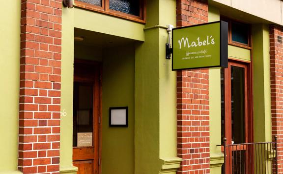 The storefront of Mabel's, a Burmese restaurant in Te Aro, Wellington. It is a red-brick building with olive-green accents. 