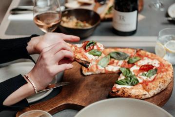 A pair of hands pick up a slice of Marguerita pizza at The Runholder's restaurant and tasting room in Martinborough.