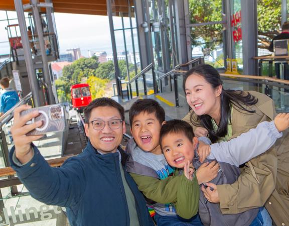 A family of four takes a selfie at the Wellington Cable Car at the Kelburn Terminal.