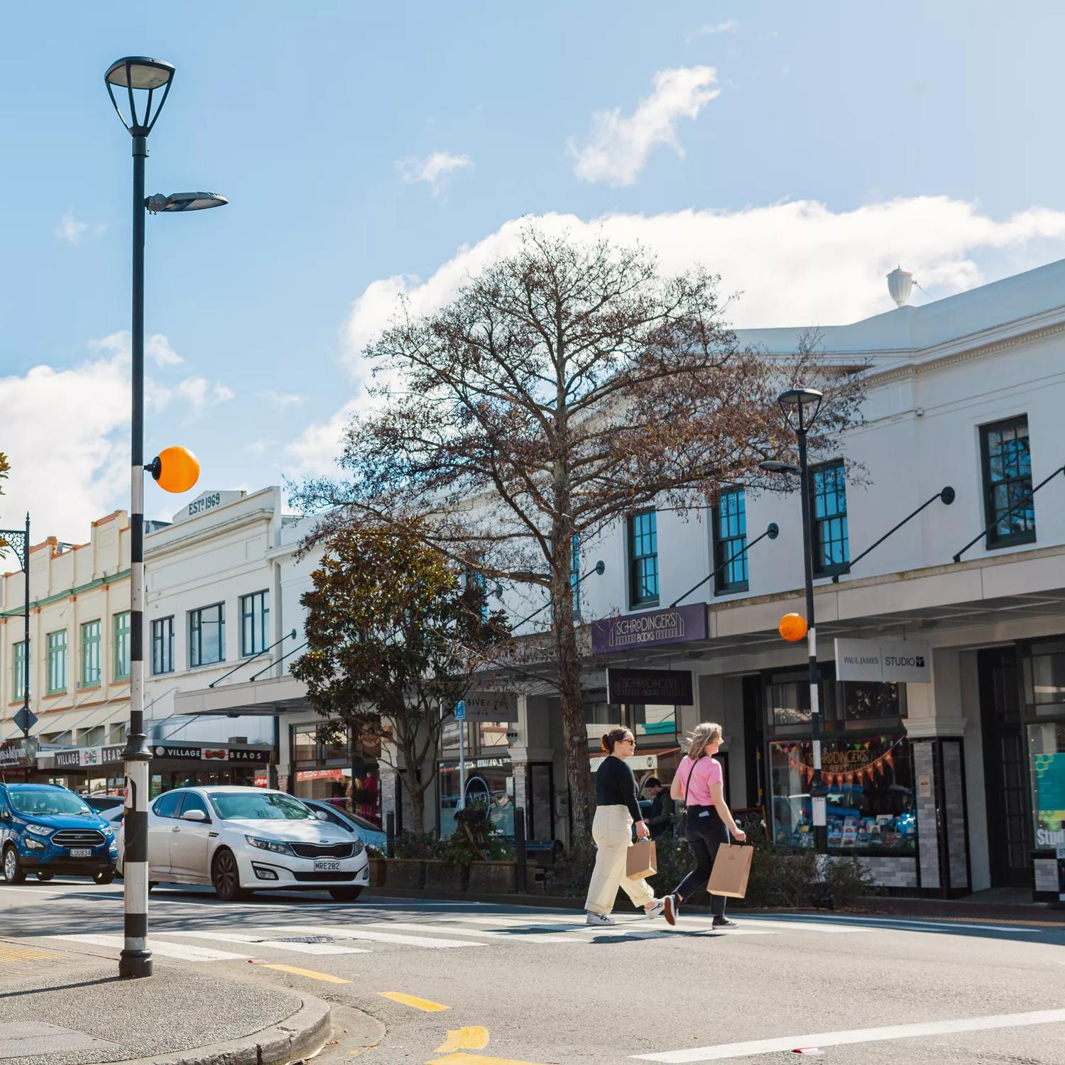 Heritage building facades line Jackson Street in Petone, as two people cross the pedestrian crossing with shopping bags.