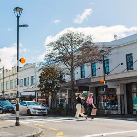Heritage building facades line Jackson Street in Petone, as two people cross the pedestrian crossing with shopping bags.