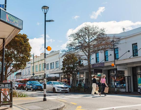 Heritage building facades line Jackson Street in Petone, as two people cross the pedestrian crossing with shopping bags.