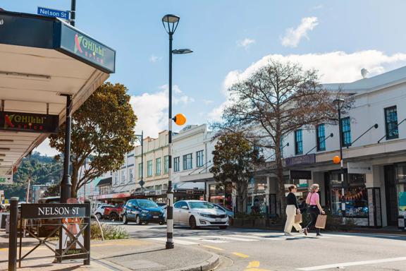 Heritage building facades line Jackson Street in Petone, as two people cross the pedestrian crossing with shopping bags.