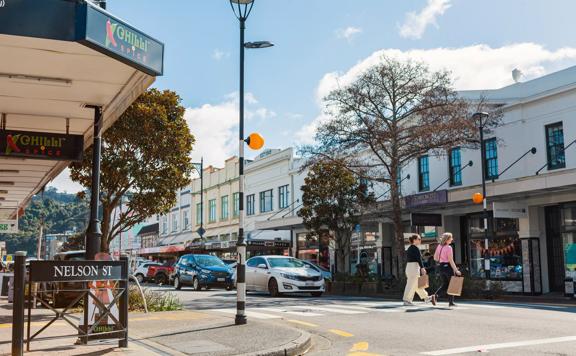 Heritage building facades line Jackson Street in Petone, as two people cross the pedestrian crossing with shopping bags.