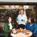 A smiling server brings a couple of coffees to two friends at a patio table.