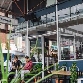 Four friends enjoy coffees at a table outside of Swimsuit on Dixon Street in Te Aro, Wellington.