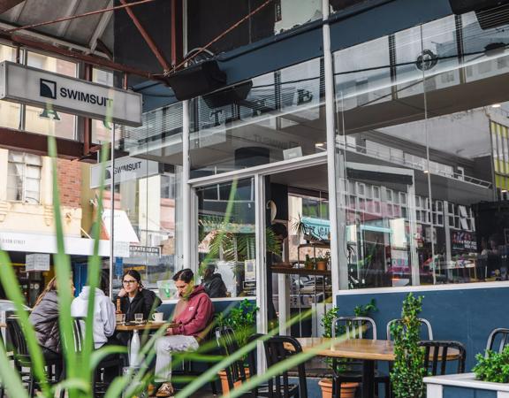 Four friends enjoy coffees at a table outside of Swimsuit on Dixon Street in Te Aro, Wellington.