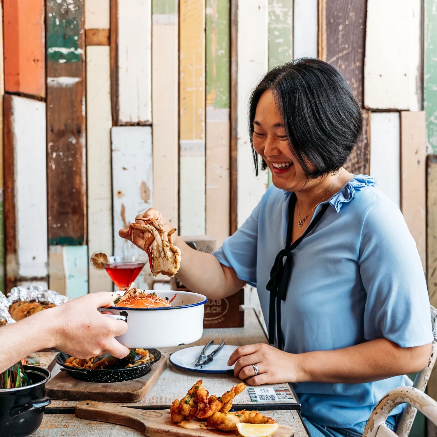 Three people eat crab and other seafood plates at The Crab Shack on Queens Wharf.