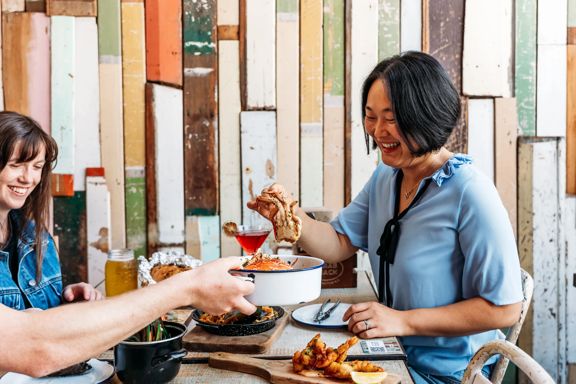 Three people eat crab and other seafood plates at The Crab Shack on Queens Wharf.