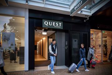 Three travellers walk out of a hotel with suitcases in hand.