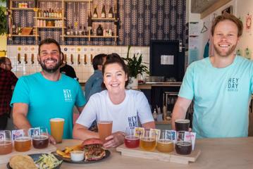 Three smiling people wearing matching tee-shirts and enjoying food and beers at Heyday Beer Co.